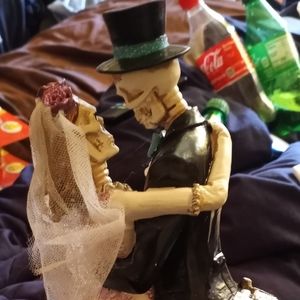 Bride and groom statue as skeletons slow dancing in front of a gravestone